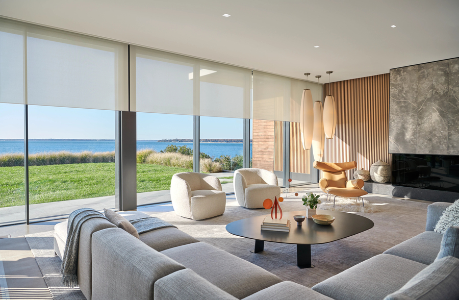 A living room with a view of the water. Lutron’s shades are partially lowered over the windows, and sunlight is filtering through.