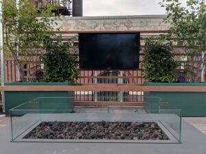 Rooftop deck with wood lounge chairs, modern railing, and expansive city and water views under cloudy skies.