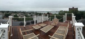 Rooftop setup with glass fire pit, mounted TV, potted greenery, and industrial building backdrop for urban relaxation.