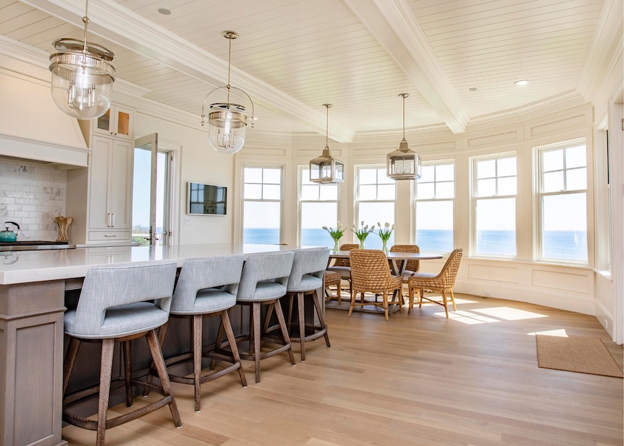 Brightly lit kitchen with island, pendant lights, and a bay-window dining alcove. A framed digital calendar is on the wall.